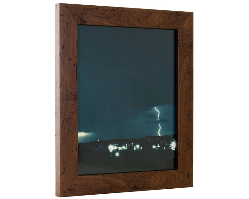 May include: A dark wood picture frame with a photograph of a city skyline at night with a lightning bolt in the sky.