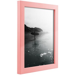 May include: A pink picture frame with a black and white photo of a person surfing in the ocean.