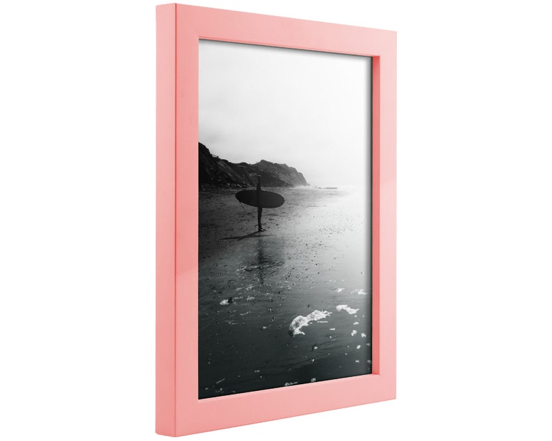 May include: A pink picture frame with a black and white photo of a person surfing in the ocean.