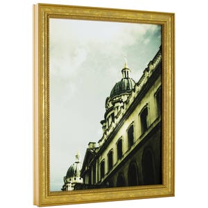 May include: A framed photograph of a building with a dome-shaped roof. The building is made of stone and has a lot of windows. The photo is in a gold frame with a decorative border.