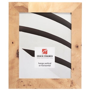 May include: A natural wood picture frame with a light brown finish. The frame has a beveled edge and a simple design. It hangs vertically or horizontally. "Craig Frames" and "www.craigframes.com" are printed on the mat.