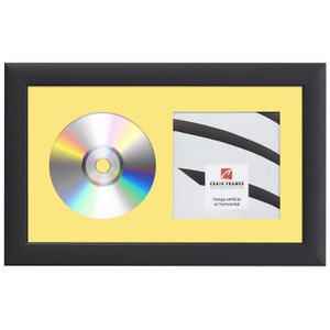 May include: Black picture frame with a yellow mat and a CD and a smaller square opening. The text on the smaller opening reads "Craig Frames www.craigframes.com hangs vertical or horizontal".