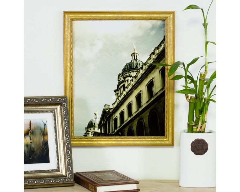 May include: A gold-colored picture frame with a black and white photograph of a building with a dome. The frame has a decorative border.