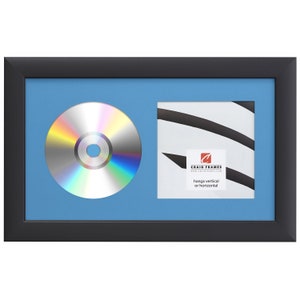 May include: Black picture frame with a blue mat and a CD and a square opening for a photo. The frame has a label that says "Craig Frames" and "hangs vertical or horizontal".