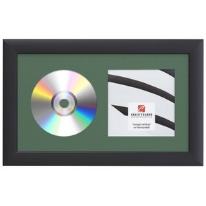 May include: Black picture frame with a green mat and a CD and a white card with black stripes and the text "Craig Frames www.craigframes.com hangs vertical or horizontal".