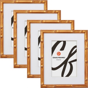 May include: Set of three gold bamboo picture frames with white mounts. The frames are nested inside each other, with the largest frame at the back and the smallest frame at the front. The frames are made of a wood-like material with a gold finish. The mounts are white and have a bevelled edge. The frames are all the same size and shape. The frames are perfect for displaying photos, artwork, or other decorative items.