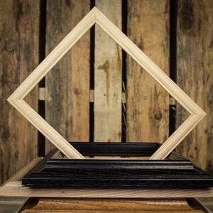 May include: A wooden picture frame with a black and brown wood base. The frame is made of light wood and has a diamond shape. The frame is sitting on a wooden surface.