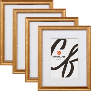 May include: Set of four gold picture frames with a white mat and a simple, elegant design. The frames are made of wood and have a slightly textured finish. The frames are arranged in a staggered pattern, with the largest frame in the back and the smallest frame in the front. The frames are all empty, ready to be filled with your favorite photos or artwork.