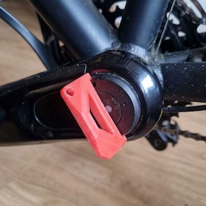 Op de afbeelding: Close-up van een zwarte fiets crankstel met een rode plastic beschermkap. Het crankstel is bevestigd aan het frame, met de ketting en versnellingen zichtbaar op de achtergrond. De fiets lijkt in goede staat te verkeren.