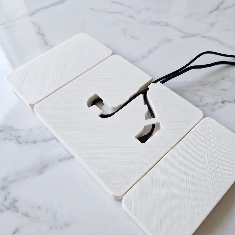 May include: A white, geometric phone charging pad with a cutout design and a black cord. The pad is composed of several rectangular pieces, arranged to create a unique shape. The design is minimalist and modern.