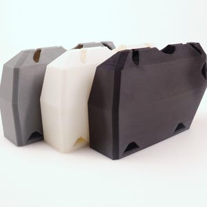 K&ouml;nnte beinhalten: Drei 3D-gedruckte Aufbewahrungsbeh&auml;lter in einer Reihe. Die Beh&auml;lter sind grau, wei&szlig; und schwarz. Jeder hat eine trapezf&ouml;rmige Form mit einem Schlitz oben und dreieckigen Aussparungen an den unteren Ecken. Hergestellt aus mattem Kunststoff.