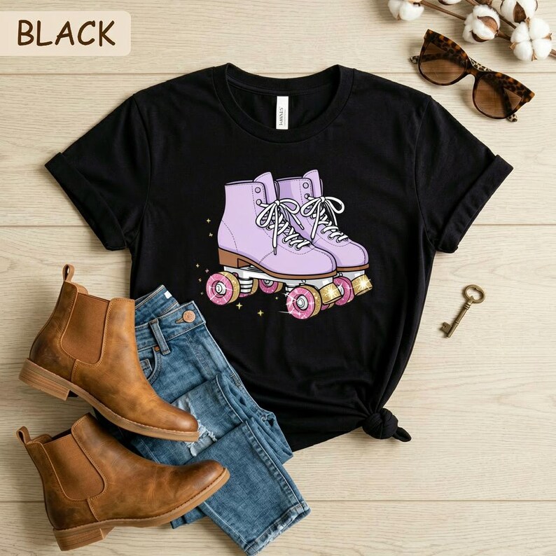May include: Black t-shirt featuring a graphic of lavender roller skates with pink donut wheels. The shirt is paired with blue jeans and brown ankle boots. The word "BLACK" is printed at the top left.