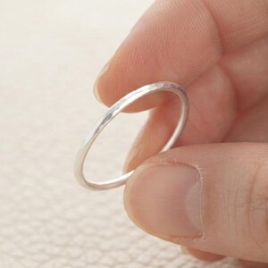 Könnte beinhalten: Ein dünner, polierter silberfarbener Ring mit einer glatten, abgerundeten Oberfläche. Der Ring zeichnet sich durch ein schlichtes, minimalistisches kreisförmiges Design mit einer reflektierenden metallischen Oberfläche aus, die eine gleichmäßige Dicke aufweist.