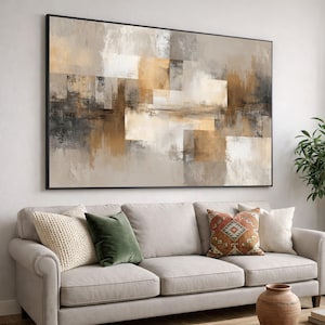 May include: A large rectangular wall art piece featuring an abstract composition of overlapping geometric blocks in shades of beige, cream, white, charcoal gray, and metallic gold, all enclosed within a thin black frame mounted on a wall.