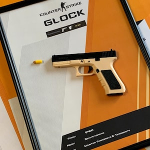 May include: Framed artwork featuring a replica Glock pistol with a yellow bullet. The artwork includes the text "COUNTER STRIKE" and "GLOCK". The background is orange and white with text indicating the price and mode.