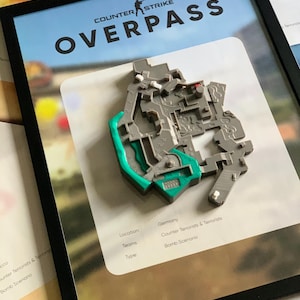 May include: A framed 3D map of the Counter-Strike Overpass level. The gray and teal plastic map is mounted on a white background with text reading Location: Germany, Teams: Counter Terrorists & Terrorists, and Type: Bomb Scenario in a black frame.