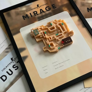 May include: Framed artwork featuring a 3D model of the "Mirage" map from Counter-Strike. The map is tan with green and brown accents, set against a blurred background. The frame is black, and the text "COUNTER STRIKE MIRAGE" is visible.