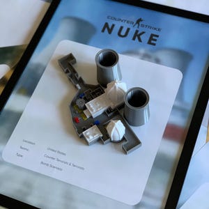 May include: A 3D-printed model of the Counter-Strike Nuke map featuring two grey cooling towers, white buildings, and small colored markers on a white card. The card displays the text Counter-Strike Nuke, Location: United States, Teams: Counter Terrorists & Terrorists, and Type: Bomb Scenario.