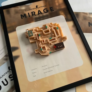 May include: A framed 3D wall art piece featuring the Counter-Strike Mirage map. The beige plastic model displays the layout with small teal and red accents. Text reads: Counter-Strike Mirage, Location: Morocco, Teams: Counter-Terrorists & Terrorists, Type: Bomb Scenario.