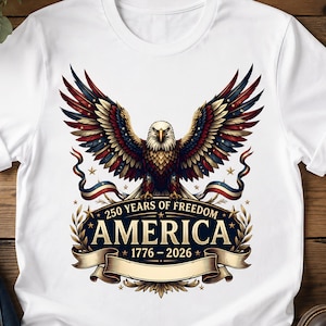 May include: A white t-shirt featuring a graphic of a bald eagle with wings spread, colored in red, white, and blue. Below the eagle is a banner with the text 250 YEARS OF FREEDOM, AMERICA, and 1776 - 2026, surrounded by gold stars and laurel leaves.