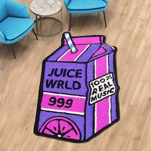以下が含まれることがあります： ジュースボックスの形をした紫とピンクのJuice WRLD 999ラグ。テキスト「100％Real Music」が書かれています。2つの青い椅子と小さな丸いテーブルが背景にあります。ラグは木の床にあります。