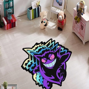May include: A purple and black rug featuring a cartoon character with a wide grin and spiky edges. The rug has a colorful design with shades of purple, blue, and yellow. The rug is placed on a light-colored wooden floor.