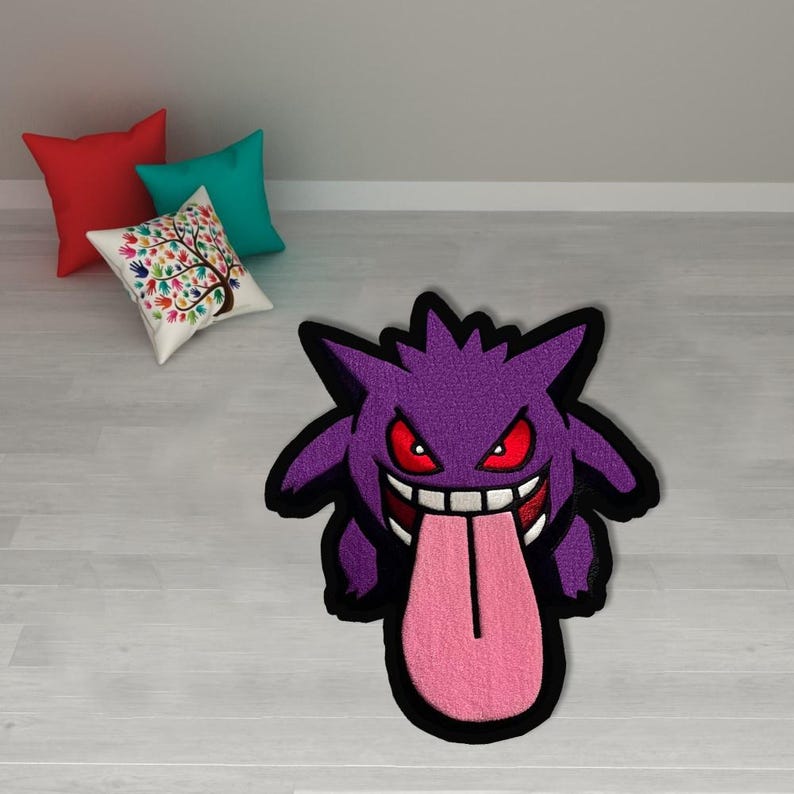 May include: A purple rug shaped like a cartoon ghost with red eyes and a long pink tongue. The rug has a black border. Three throw pillows in red, teal, and a white pillow with a tree design are in the background.