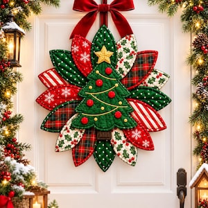 Könnte beinhalten: Ein gesteppter Stoff-Türhänger mit einem zentralen grünen Weihnachtsbaum mit roten Ornamenten und einem gelben Stern, umgeben von blattförmigen Stofflagen in Rot, Grün, Schottenkaro und Schneeflockenmustern, gekrönt von einer großen roten Samtschleife.