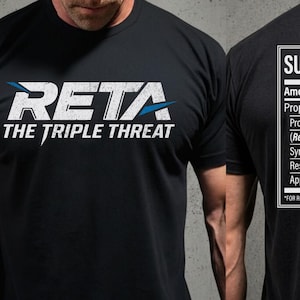 May include: Black t-shirt with the text "RETA THE TRIPLE THREAT" in white and blue. The back of the shirt displays a "SUPPLEMENT FACTS" label with ingredient information, including "Retatrutide-inspired Analogs".