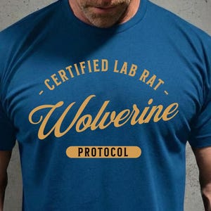 May include: A blue t-shirt with the text "CERTIFIED LAB RAT - Wolverine PROTOCOL" in yellow. The text is arched above the word "Wolverine" in a cursive font, with "PROTOCOL" in a rectangular box below.