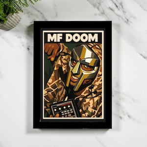 May include: A framed art print featuring MF DOOM. The artwork shows a masked figure in a camouflage jacket holding a device. The words "MF DOOM" are printed in bold white letters at the top of the frame. The frame is black.