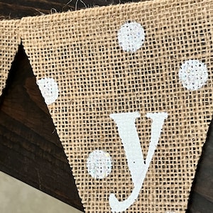 This photo shows an adorable gender neutral triangular flag baby banner perfect for a baby shower. The letters are hand painted in white. There are white polka dots with iridescent glitter paint on every flag.