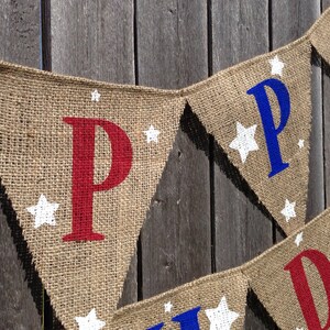 This is a burlap banner that says happy birthday. The letters are hand painted in alternating blue and red letters. There are three to four white stars of different sizes on each flag.