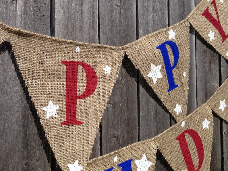 This is a burlap banner that says happy birthday. The letters are hand painted in alternating blue and red letters. There are three to four white stars of different sizes on each flag.