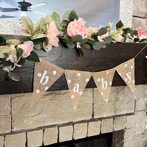 This photo shows an adorable gender neutral triangular flag baby banner perfect for a baby shower. The letters are hand painted in white. There are white polka dots with iridescent glitter paint on every flag.