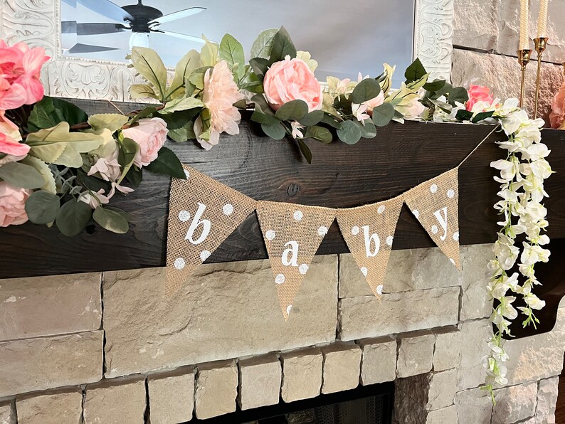 This photo shows an adorable gender neutral triangular flag baby banner perfect for a baby shower. The letters are hand painted in white. There are white polka dots with iridescent glitter paint on every flag.