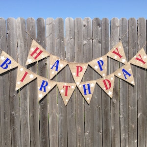 This is a burlap banner that says happy birthday. The letters are hand painted in alternating blue and red letters. There are three to four white stars of different sizes on each flag.