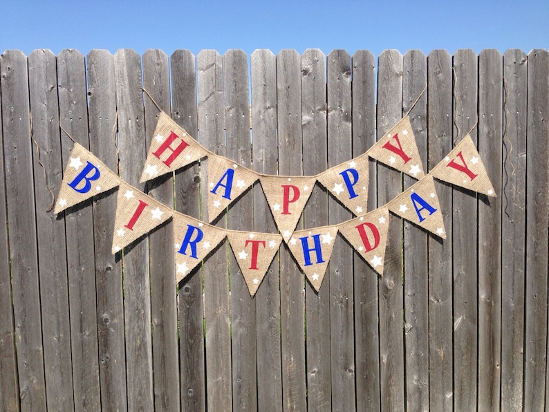 This is a burlap banner that says happy birthday. The letters are hand painted in alternating blue and red letters. There are three to four white stars of different sizes on each flag.