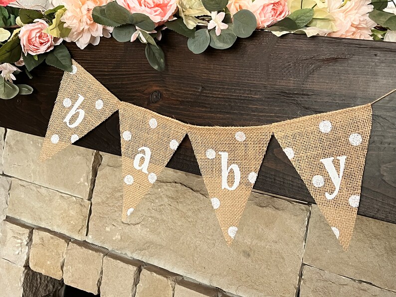 This photo shows an adorable gender neutral triangular flag baby banner perfect for a baby shower. The letters are hand painted in white. There are white polka dots with iridescent glitter paint on every flag.