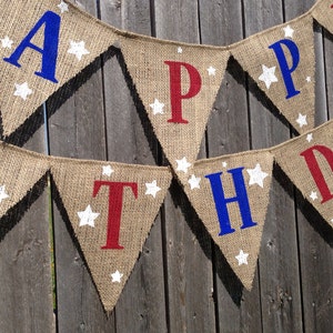 This is a burlap banner that says happy birthday. The letters are hand painted in alternating blue and red letters. There are three to four white stars of different sizes on each flag.