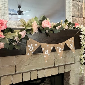 This photo shows an adorable gender neutral triangular flag baby banner perfect for a baby shower. The letters are hand painted in white. There are white polka dots with iridescent glitter paint on every flag.