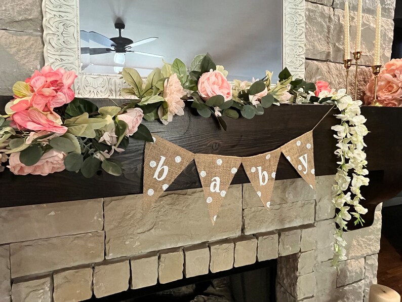 This photo shows an adorable gender neutral triangular flag baby banner perfect for a baby shower. The letters are hand painted in white. There are white polka dots with iridescent glitter paint on every flag.