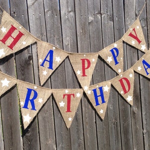 This is a burlap banner that says happy birthday. The letters are hand painted in alternating blue and red letters. There are three to four white stars of different sizes on each flag.