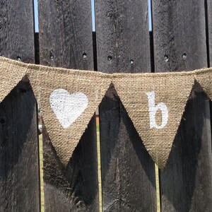 May include: A burlap banner with white painted letters spelling "Happy" and a heart, followed by the letters "b" and "a".