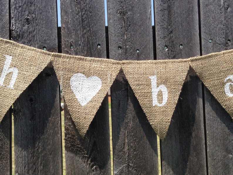 May include: A burlap banner with white painted letters spelling "Happy" and a heart, followed by the letters "b" and "a".