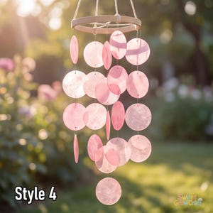 May include: A hanging mobile featuring multiple translucent, circular pink discs suspended from a light-coloured wooden hoop by thin white strings. The discs vary in size and are arranged in vertical strands. The text Style 4 is visible.