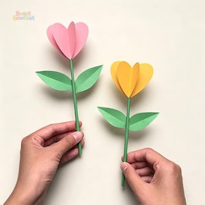 May include: Two paper flowers with heart-shaped petals in pink and yellow, each attached to a green stem with two green leaves. The text Sweet GrowCraft is visible in the top left corner. The flowers are constructed from layered cardstock.