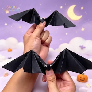 以下が含まれることがあります： 折り紙で作られた2匹の黒いコウモリ。それぞれに黒い瞳の小さな白い動く目が付いています。コウモリには尖った耳と角張ったプリーツ状の翼があり、正確な折り紙技術によって作られたシャープで幾何学的なデザインが特徴です。