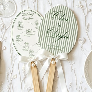 May include: Two oval-shaped hand fans with wooden handles. One fan features a green and white striped pattern with the text Olivia & Dylan, August 26th, 2028, Tuscany, Italy. The other displays a wedding timeline with icons and text. Both have white ribbon bows.