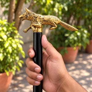 May include: A walking stick featuring a polished gold-toned metal handle shaped like a leaping wolf with detailed fur texture. The handle is mounted atop a smooth, cylindrical black shaft. The wolf is depicted in a dynamic, mid-stride pose.